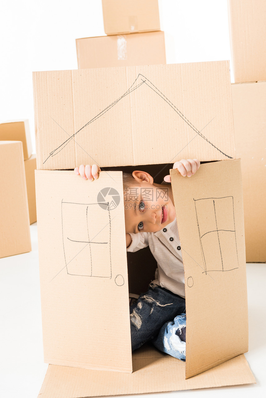 可爱的小男孩坐在纸板盒里坐着房子用白图片