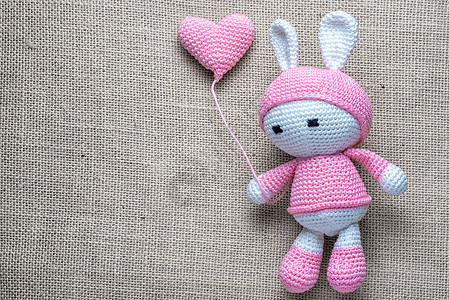 Crochet孩子的柔软玩具兔子在麻布背景上挥动毛绒气球图片