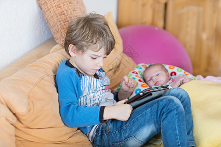 学龄前儿童男孩在保姆期间玩游戏平板电脑可爱的新生婴儿看着弟可爱的孩子图片