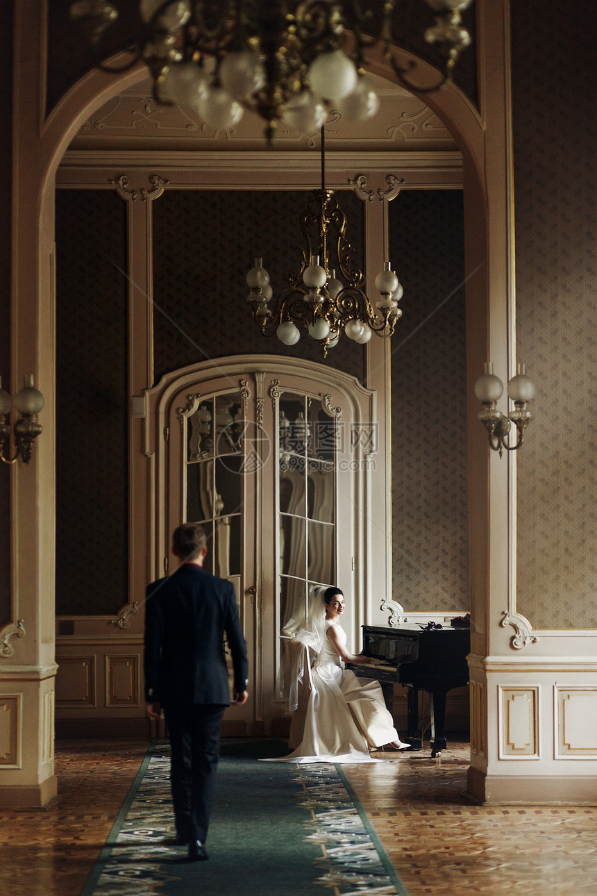 高雅的英俊帅气的新郎在弹钢琴时拥抱着他美丽的新娘图片