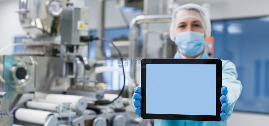 身穿蓝色实验室制服的白人科学家站在带轴的制造机器附近图片