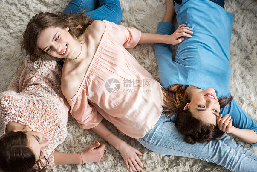 三名有吸引力的年轻妇女躺在地毯上和聊天中最图片