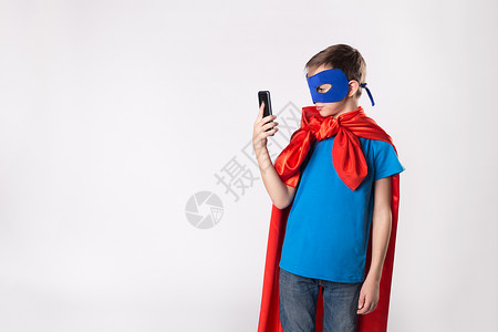 使用手机的超级英雄孩子红色斗篷和蓝色面具的超人孩子图片