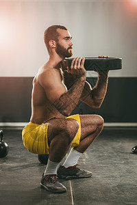 年轻的肌肉男用哑铃做蹲下运动强壮的男图片