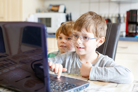 开局之年两个小男孩在电脑上玩在线棋盘游戏儿童兄弟姐妹朋友和双胞胎在电脑上玩得开背景