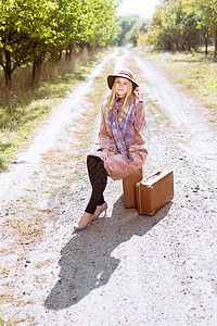 身戴帽子高雅时装外套手提箱和阳光明媚户外背景的图片