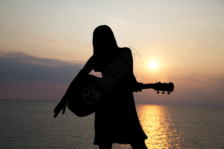 女孩在海幕和美丽的日落背景弹吉他的图片