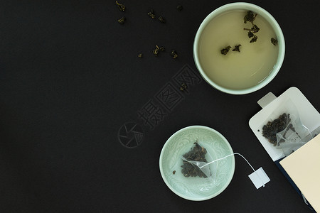 日本茶杯装着一袋茶叶的碟子和黑背景的纸图片