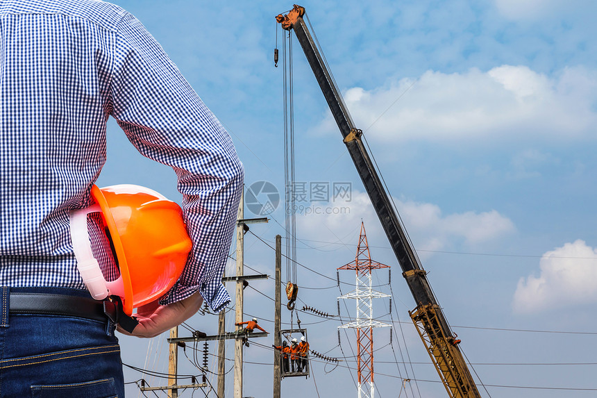 工程师在蓝天背景下用起重机在建筑工地手持黄色安全帽图片