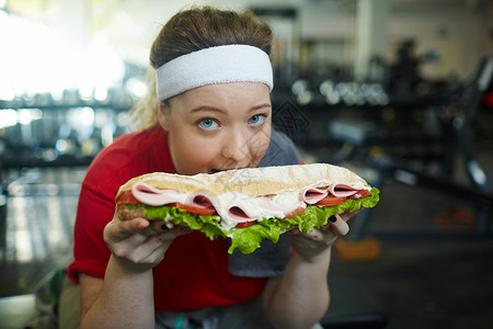 可爱超重女人的肖像被咬成大胖三明治在健身房工作图片