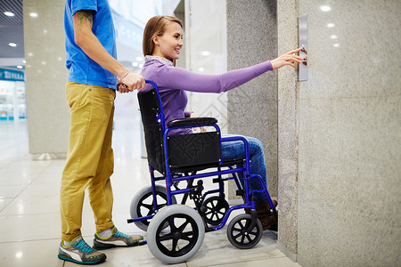 坐在轮椅上等待电梯的助理和残疾青年妇女图片