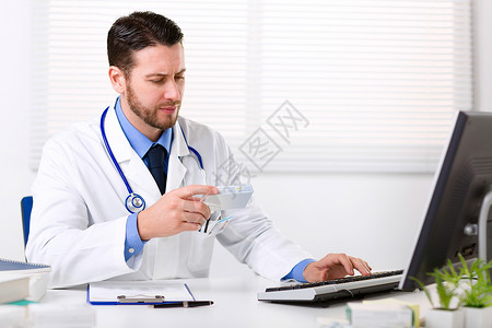身穿白大衣颈部有听诊器的男医生坐在桌子上思考处方图片