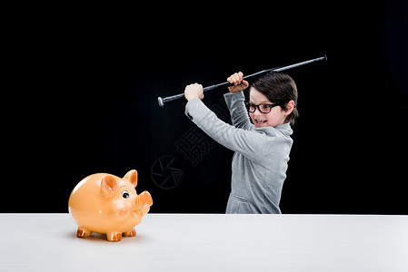 穿着正式西装的小男孩拿着棒球打小猪银行图片