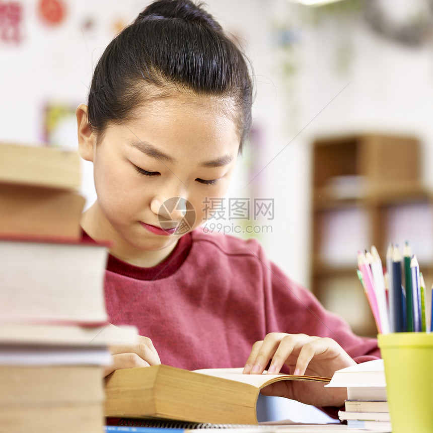 在教室里读一本厚书的亚洲小学生图片
