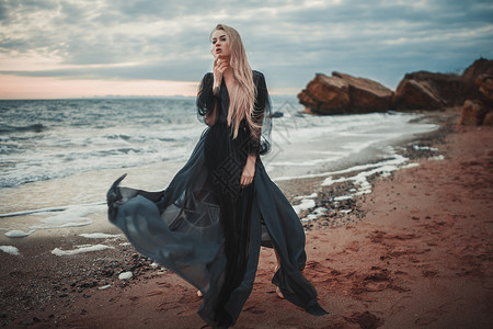 年轻女人穿长的黑色衣在海滩和海边图片