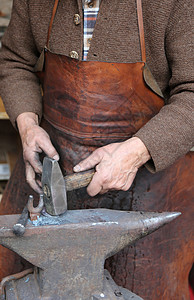 一位年长铁匠的手用锤子和铁砧打铁图片