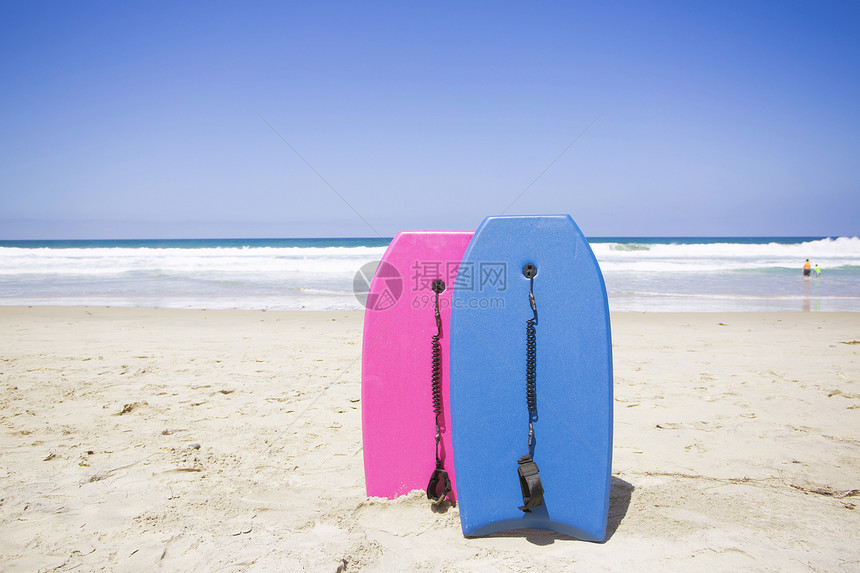 基于原始海滩的两个五颜六色的布吉板准备好在晴朗的夏日骑行并在海洋中玩乐在图片