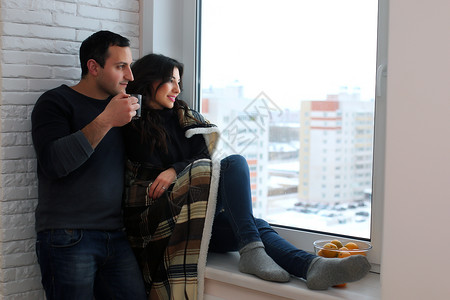 美丽的年轻夫妇看着窗外的距离窗户被裹在暖毯图片