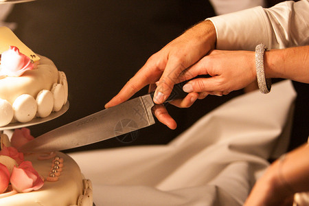 照片显示新娘和新郎在婚礼当天切结婚蛋糕的手图片