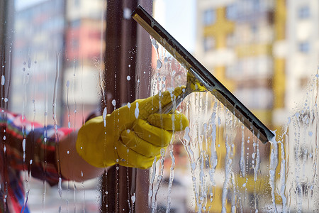 用黄色手套用手洗窗户的刮板春天洗去图片