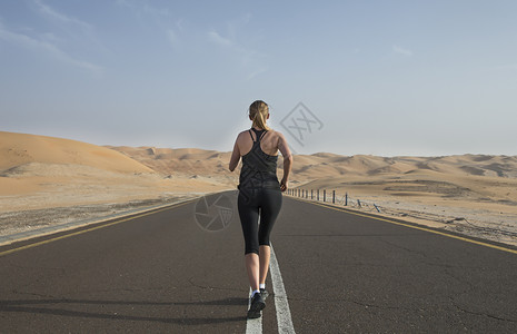 在沙漠公路上奔跑的年轻女子图片