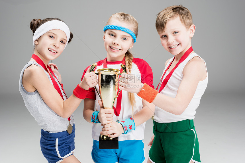 带着奖牌和高脚杯冠军的微笑的男孩与女孩在图片