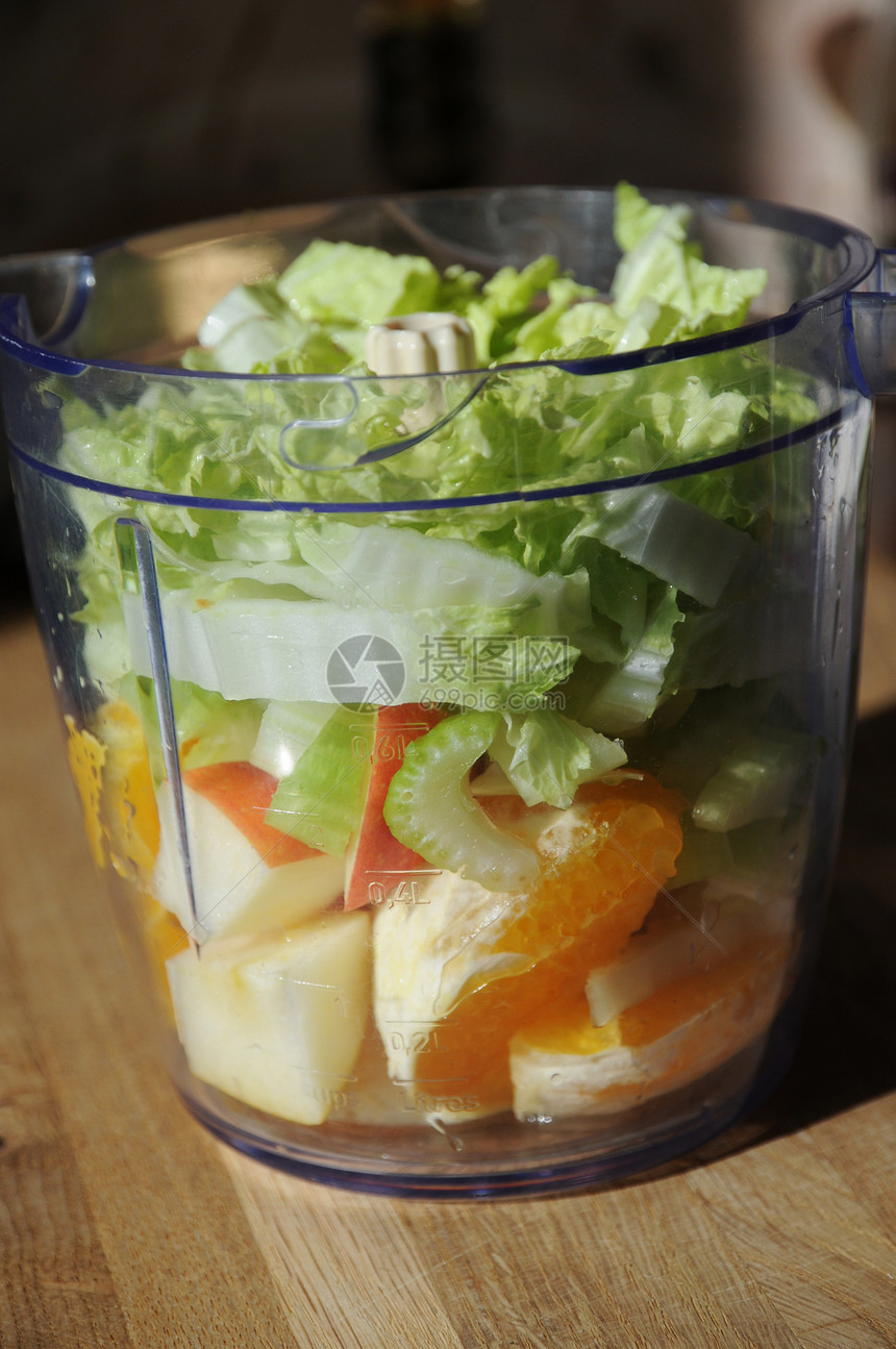 搅拌机碗中的橙子芹菜卷心菜叶和苹果冰沙的配料图片