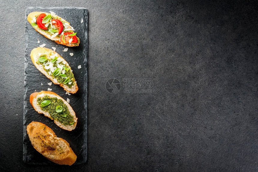 意大利食物零食开胃菜意式烤面包配香蒜酱帕尔马干酪樱桃番茄和新鲜罗勒叶在黑色石桌上图片