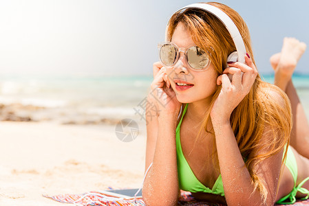 智能选基快乐的海滩女人在智能手机上放耳机听音乐暑假期间穿着比基尼的休闲女孩在手机上通过无线4g享受有趣背景