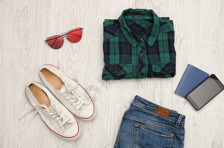 蓝绿色格子衬衫眼镜运动鞋牛仔裤电话和护照木制背景时尚图片