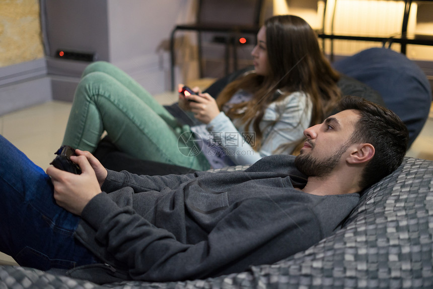 幸福的夫妇朋友用操纵杆坐在豆袋椅上玩电子游戏的画像玩家用电子游戏机图片