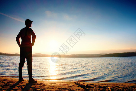 身着深色运动服背着运动背包的高个子徒步旅行者在海滩上享受日落时分图片