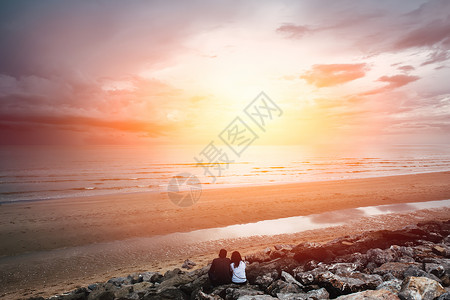 情侣们坐在沙滩上的情侣的景色着日落的光芒向大海倾斜图片