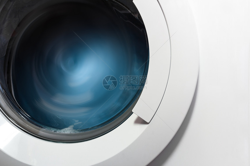 洗衣机在洗涤和旋转装有蓝色衣服的滚筒期间的舷窗的图片