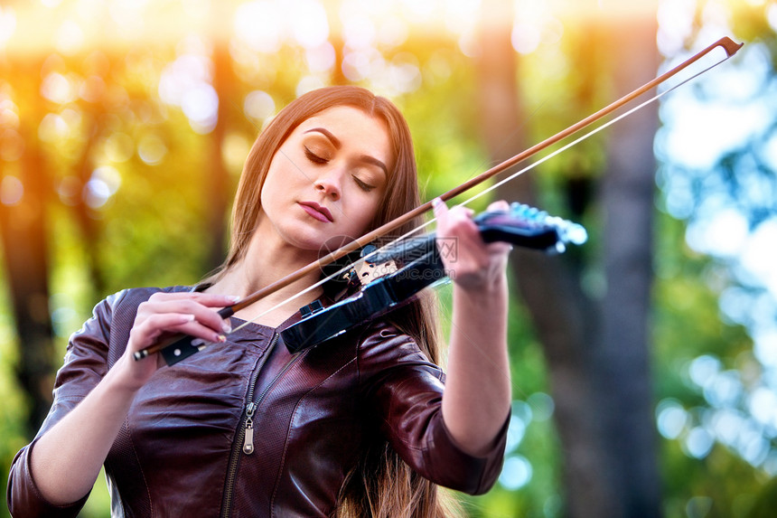 女人在户外公园用小提琴演奏音乐在城市街道上表演爵士乐的女孩春天外面有绿树启发了小提琴家的天背景图片