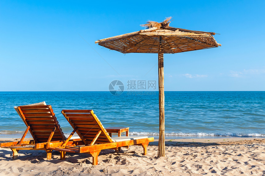 在海边沙滩上有两个防晒雨伞和稻草伞夏季的图片
