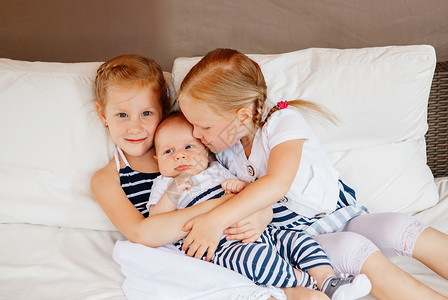 可爱的白人女孩姐妹的生活方式肖像抱着亲吻的小婴儿图片