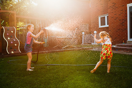 两个女孩在后院的花园房子里互相泼水孩子们在日落时在外面玩水坦率的时刻图片