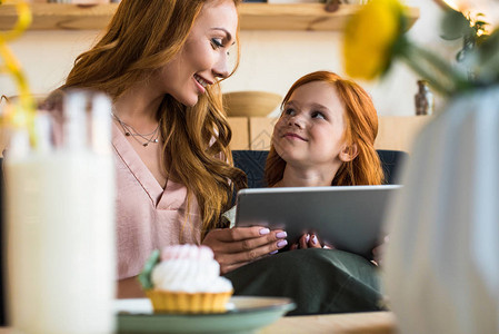 美丽的幸福母亲和女儿在咖啡馆坐在一起时使用数字平板电脑图片