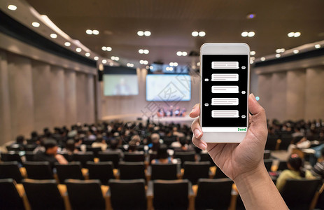女手持智能手机在模糊的会议厅或研讨室有观众背景图片
