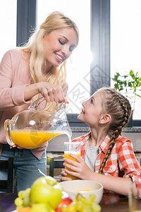 快乐的年轻母亲在早餐时倒橙汁给可图片