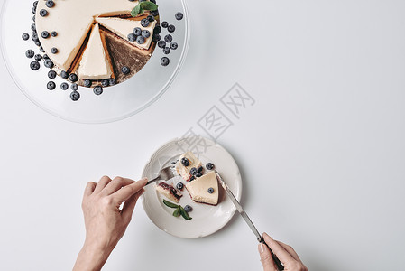 用叉子和刀子吃蓝莓芝士蛋糕的女人的顶视图图片