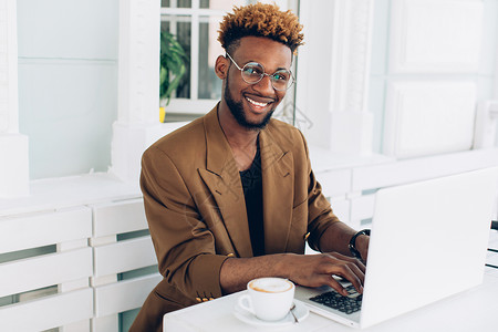 穿着夹克和眼镜的非裔美国人男子的肖像喝咖啡和在笔记图片