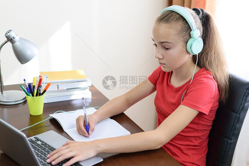 有耳机的年轻女学生正在做家庭作业或在她房间里的笔记本电图片