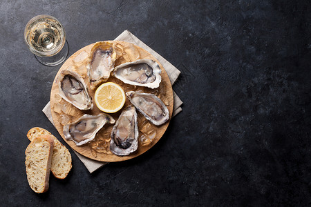 开张的牡蛎葡萄酒杯石板上的冰和柠檬图片