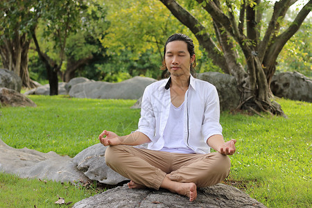 年青的瑜伽男在做瑜伽冥想时坐在公园岩石图片