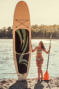 美丽的年轻美女在笑着站在沙滩上用桨板图片