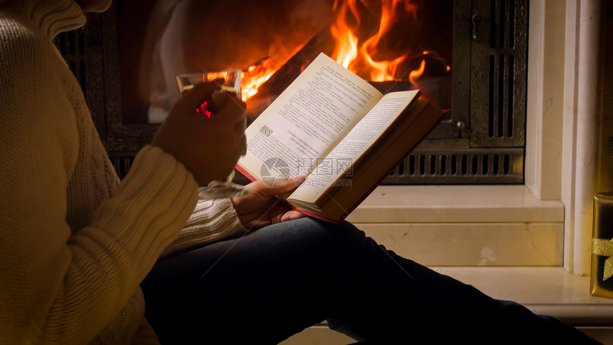 穿着白色毛衣喝茶和在壁炉阅读书的图片