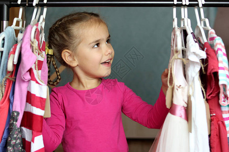 快乐可爱的学龄前女孩在儿童时装店的许多衣服中选择一件新衣服背景图片