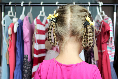 可爱的学龄前女孩在儿童时装店的许多衣服中选择一件新衣服图片